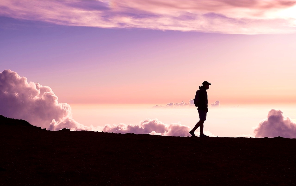 A silhouette of a person walking on a mountain under a cloudy sky.